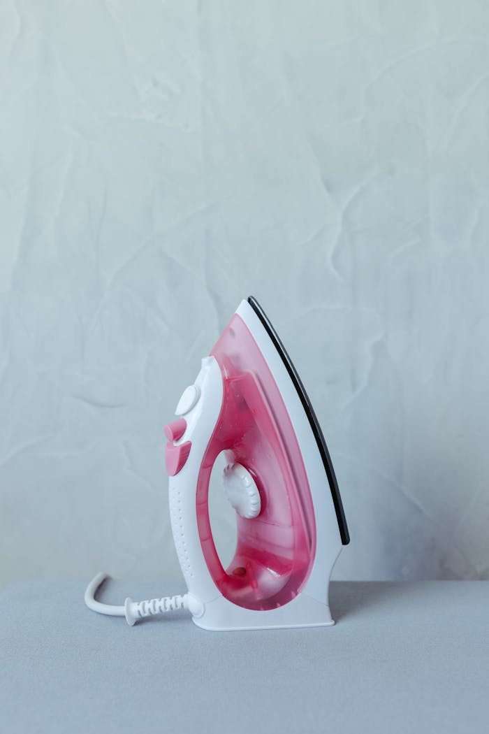 home-services-004 A pink and white electric iron displayed upright against a textured wall.
