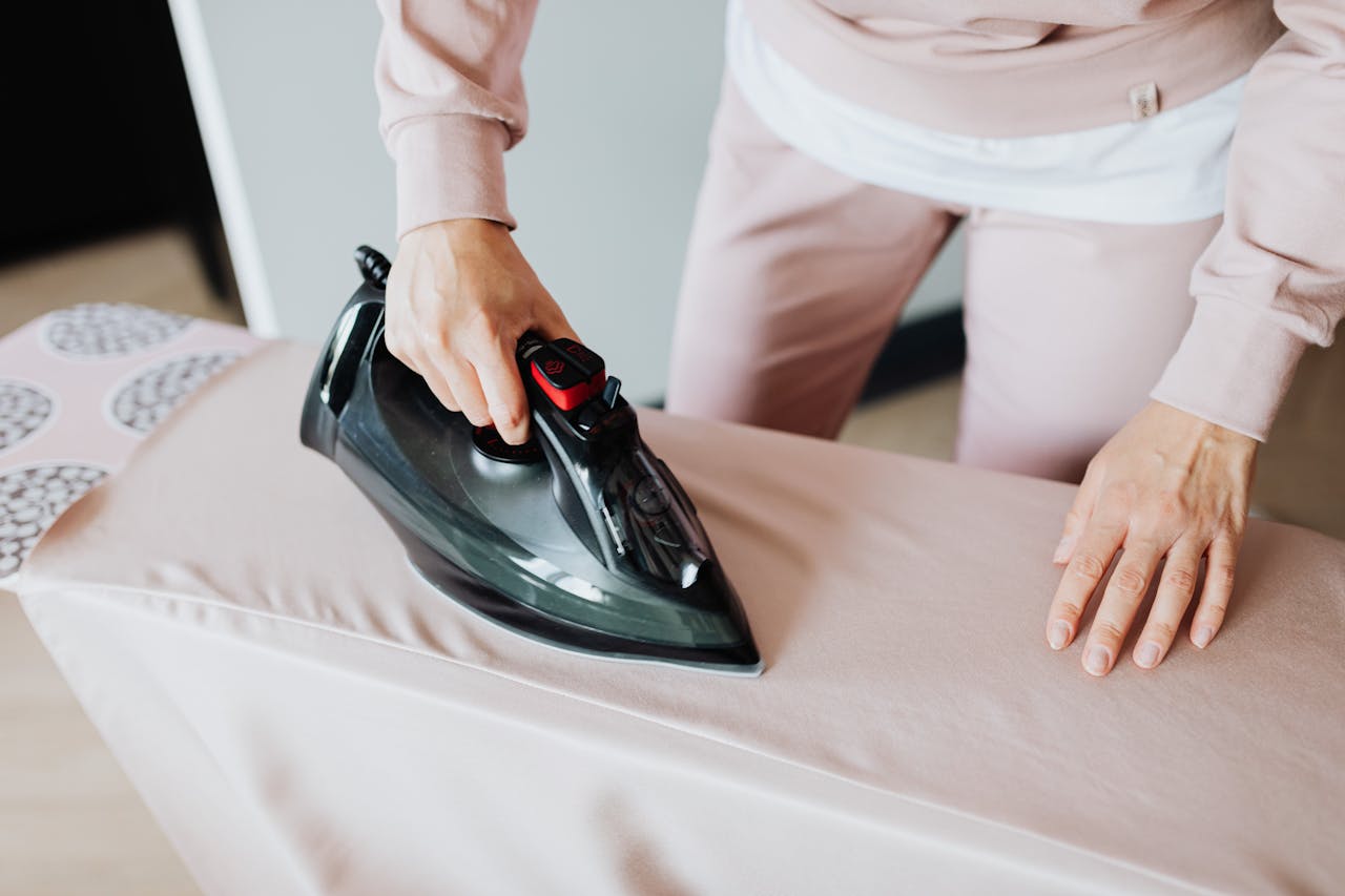 home-hero-bg Adult woman ironing clothing on board using a black iron in an indoor setting.