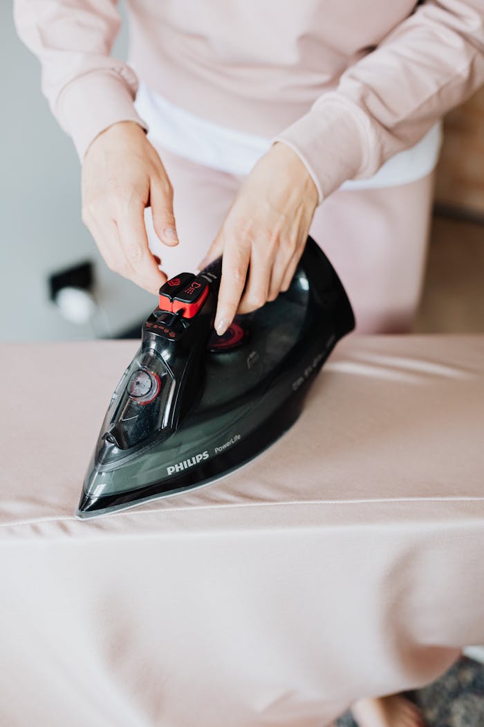 home-services-02 Close-up of a person using a Philips steam iron on a beige fabric indoors.
